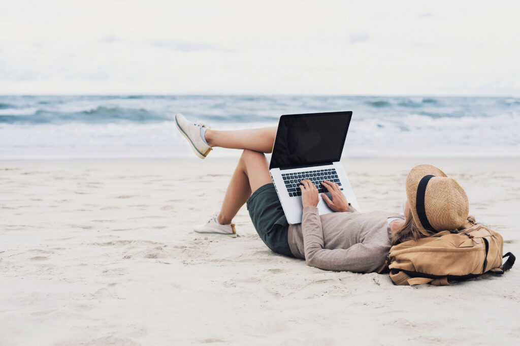Nomade digitale sdraiato sulla spiaggia a lavorare su un portatile
